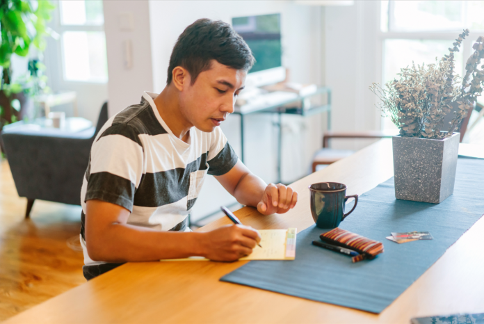 A man sits at a desk and writes on a notepad